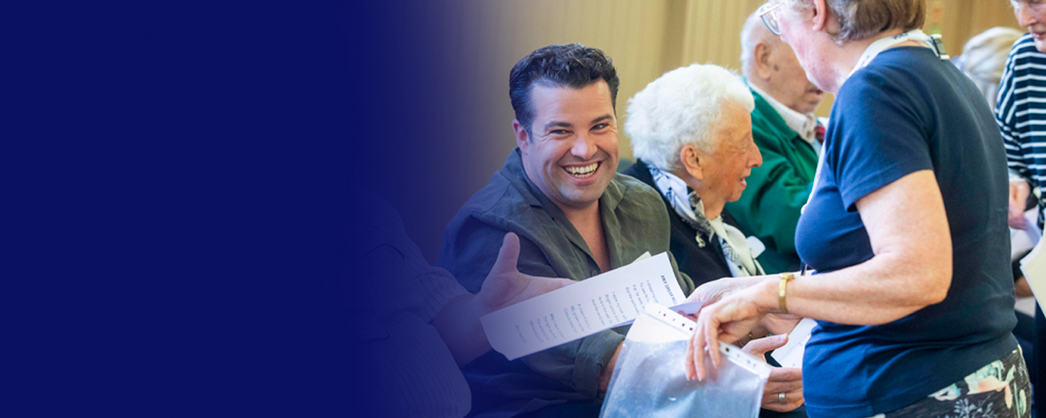 Singer Joe McElderry smiling, sat with a group of older people