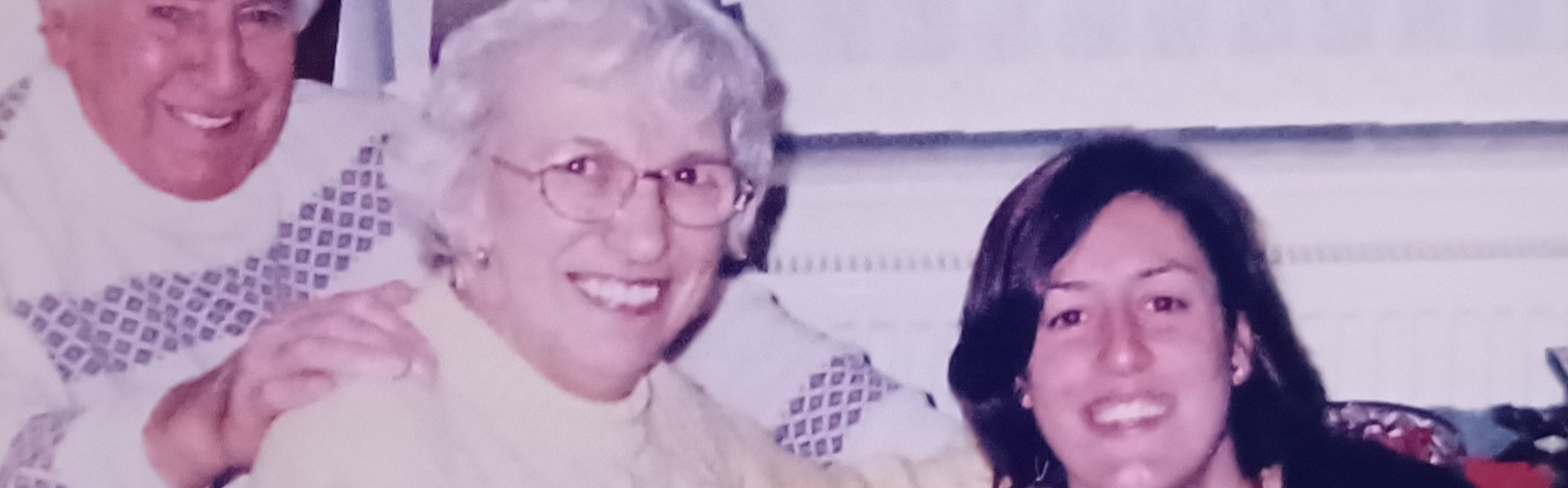 A young brunette woman smiles with her grandparents, who are wearing Christmas paper hats