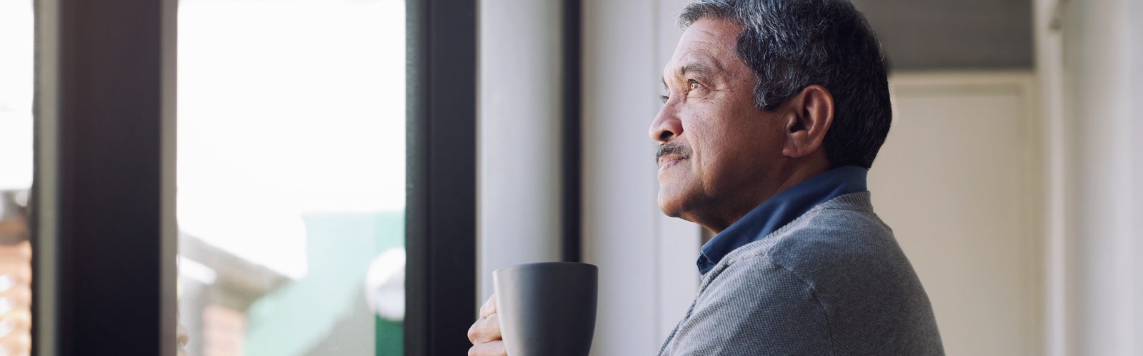 An older man staring out of the window contemplatively